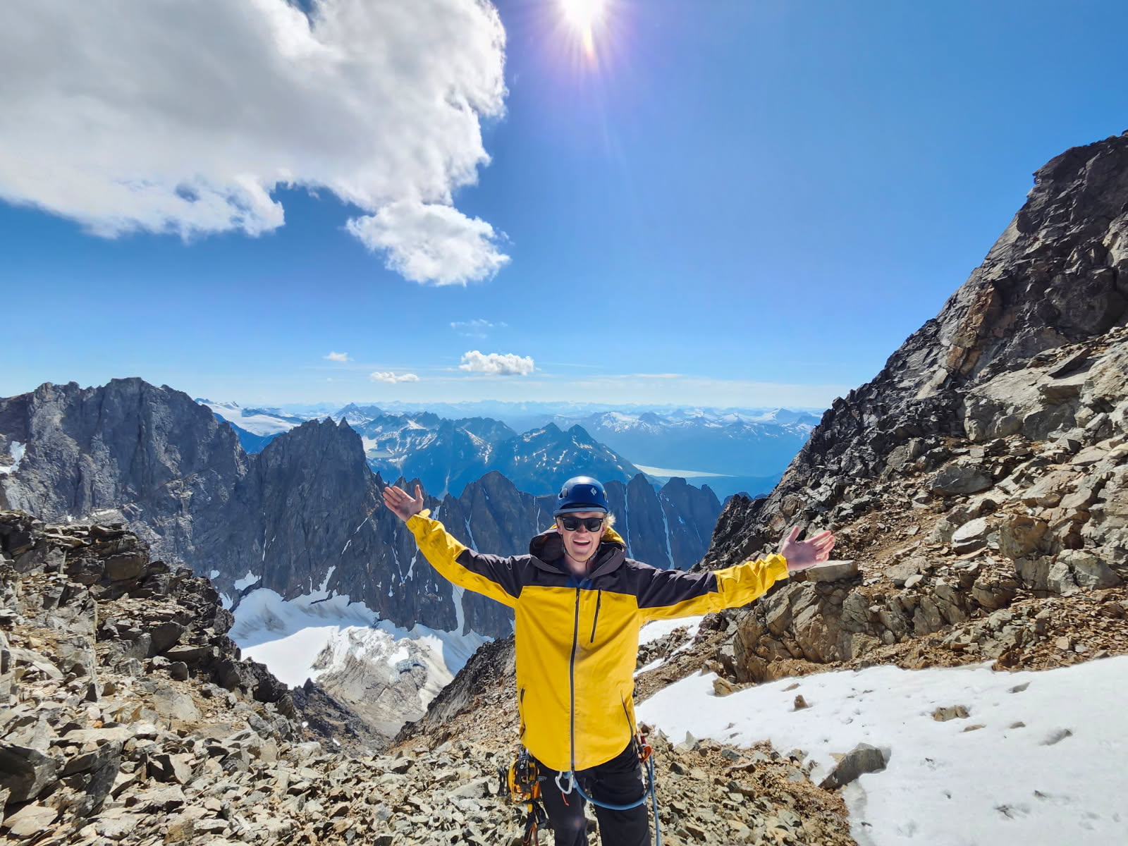 Jake Jones at the summit with arms raised, surrounded by mountain peaks